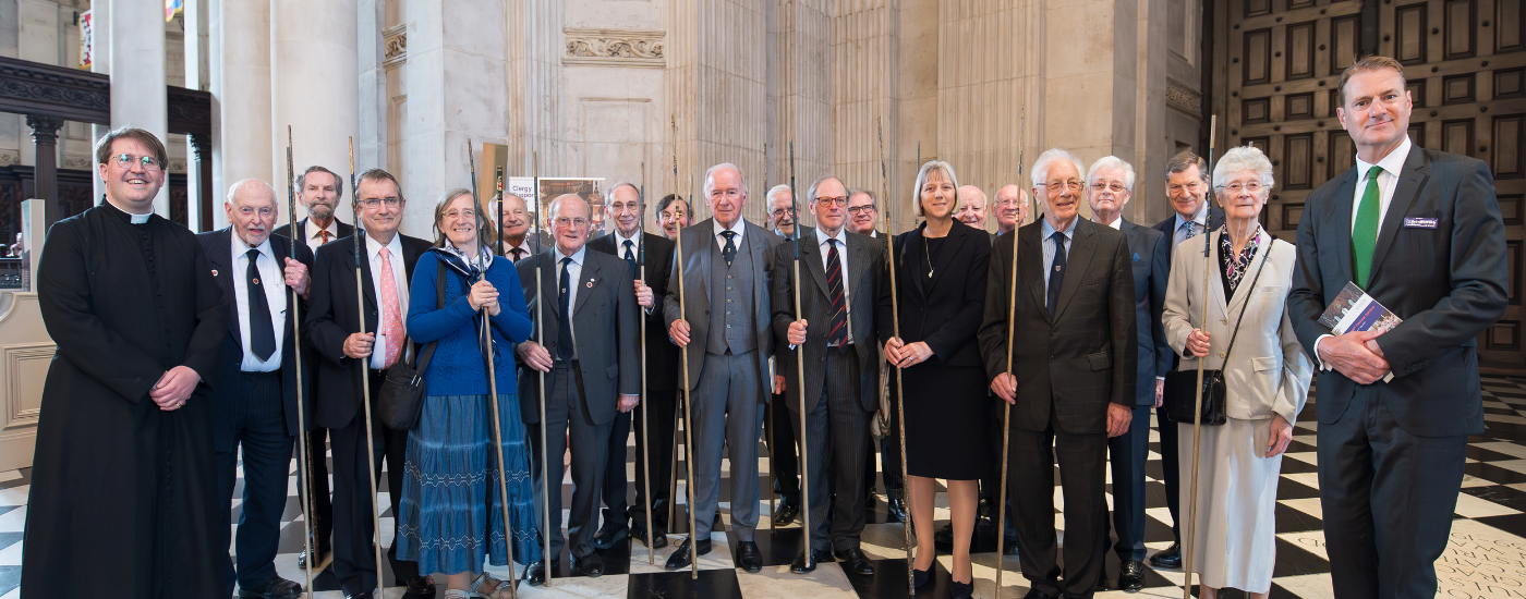 A line of formally dressed men and women, holding ceremonial sticks, known as wands.