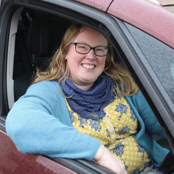 Becca, wearing a light blue cardigan, sat inside a red car, with the window open.