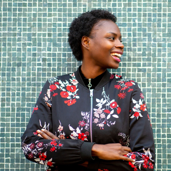 A woman wearing a colourful jacket, standing in front of a blue tiled wall.