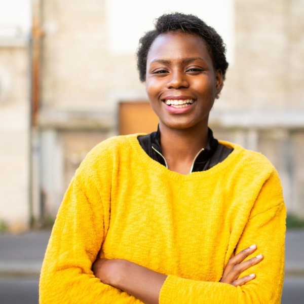 A woman wearing a yellow jumper, stood outside on a street.