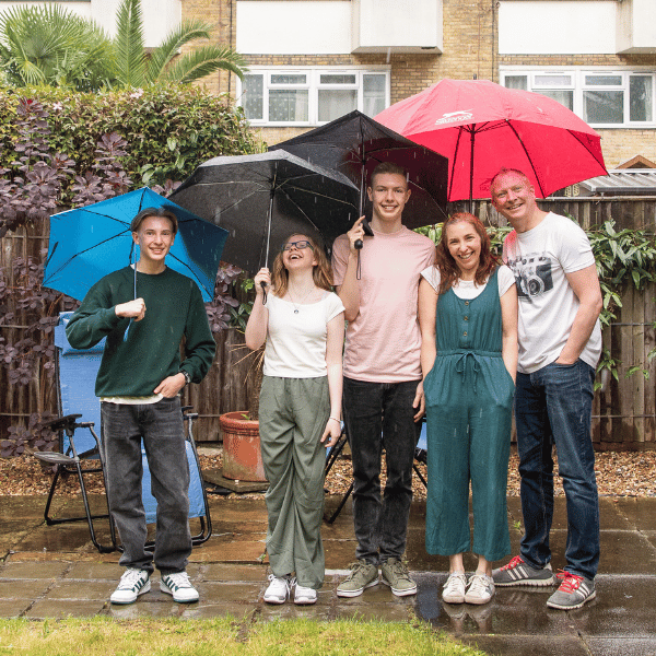 Sam, Graham and their children, stood in their back garden in the rain, under colourful umbrellas.