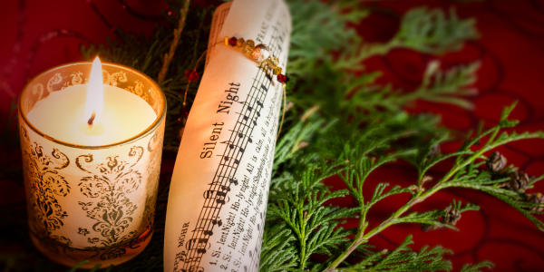 A burning candle, beside the rolled up sheet music to 'Silent Night'.