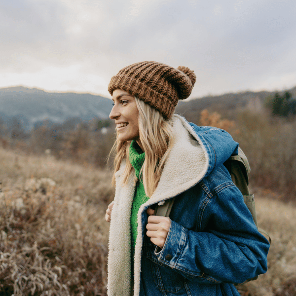 A woman enjoying a hike. She is wearing a brown bobble hat, and a blue jacket.