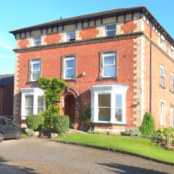 A red-bricked building, with bay windows and a long driveway.