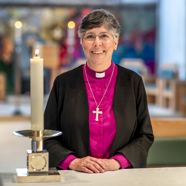 The Bishop of Chelmsford, standing in front of a lit candle, wearing a clerical collar.