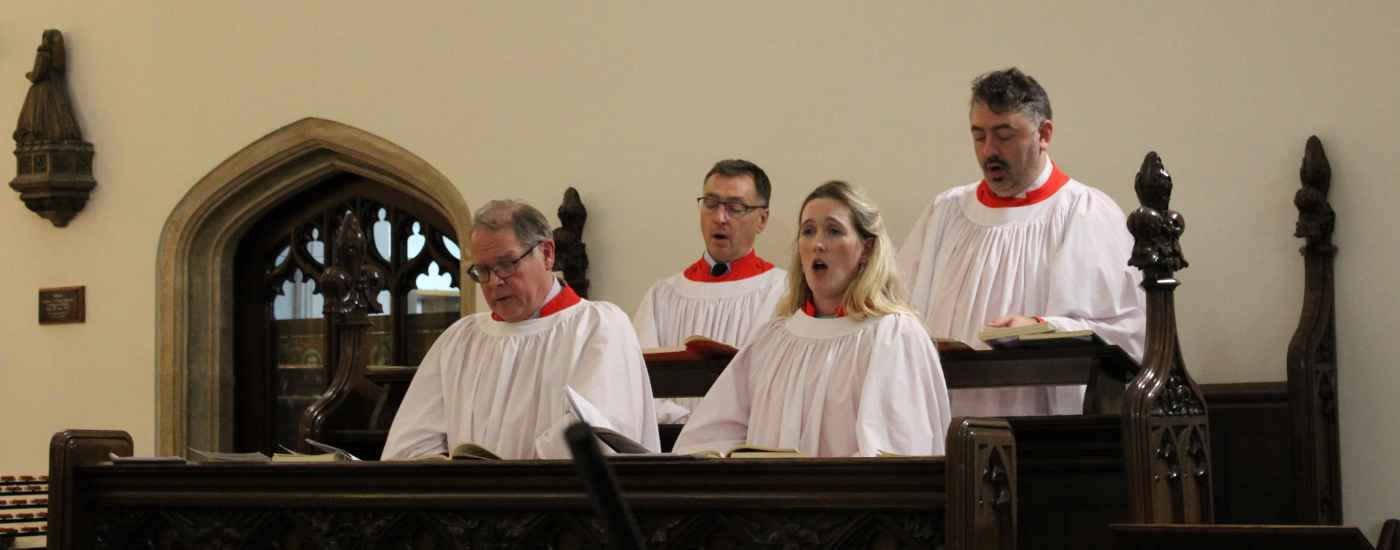 Three men and one woman, dressed in white robes, singing from the pews.