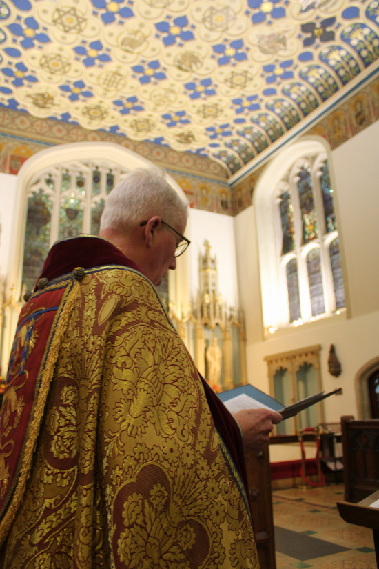 The Revd Canon Thomas Woodhouse, robed and singing from the Order of Service.