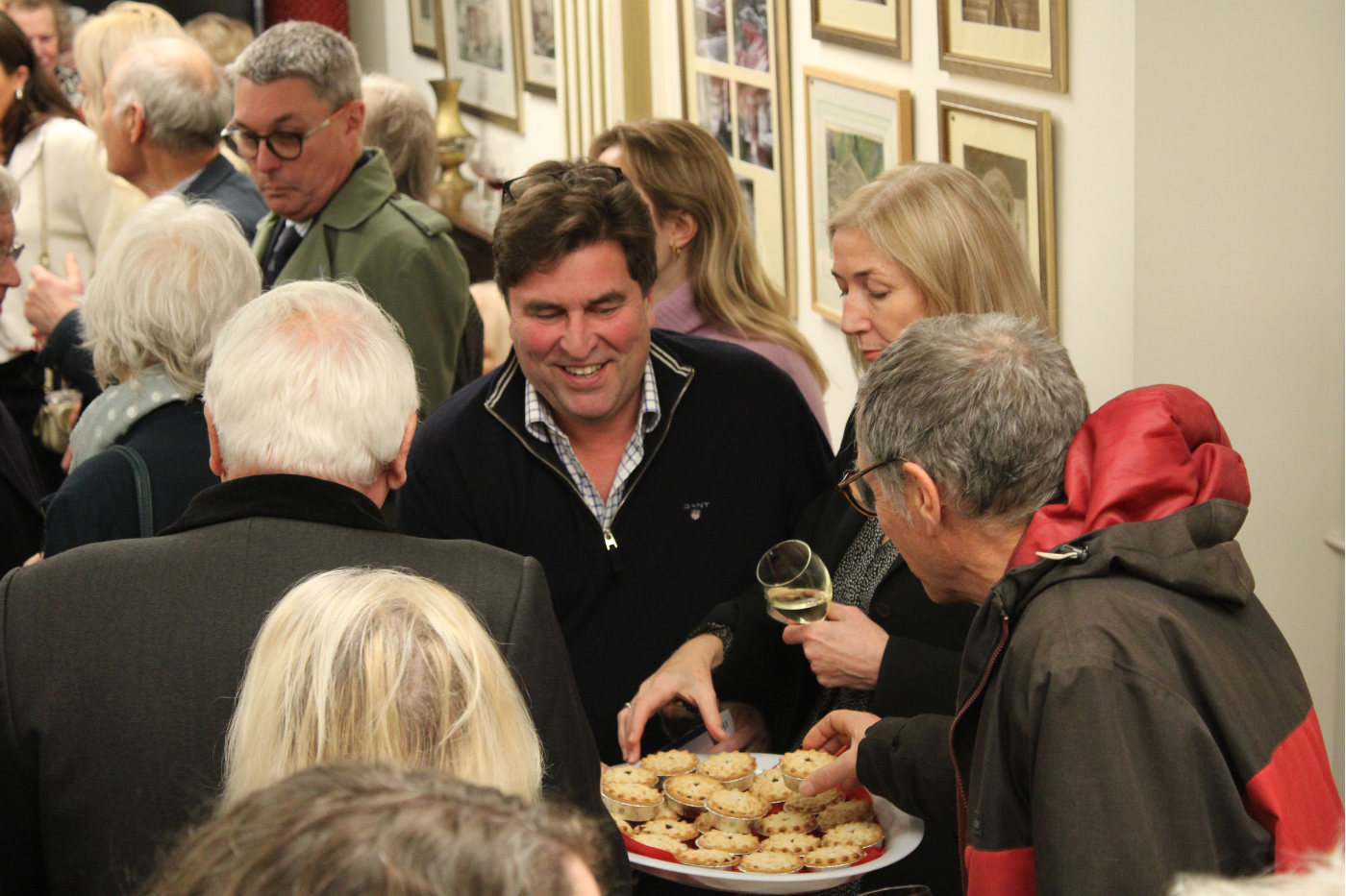 People stood around a plate of mince pies, grinning.