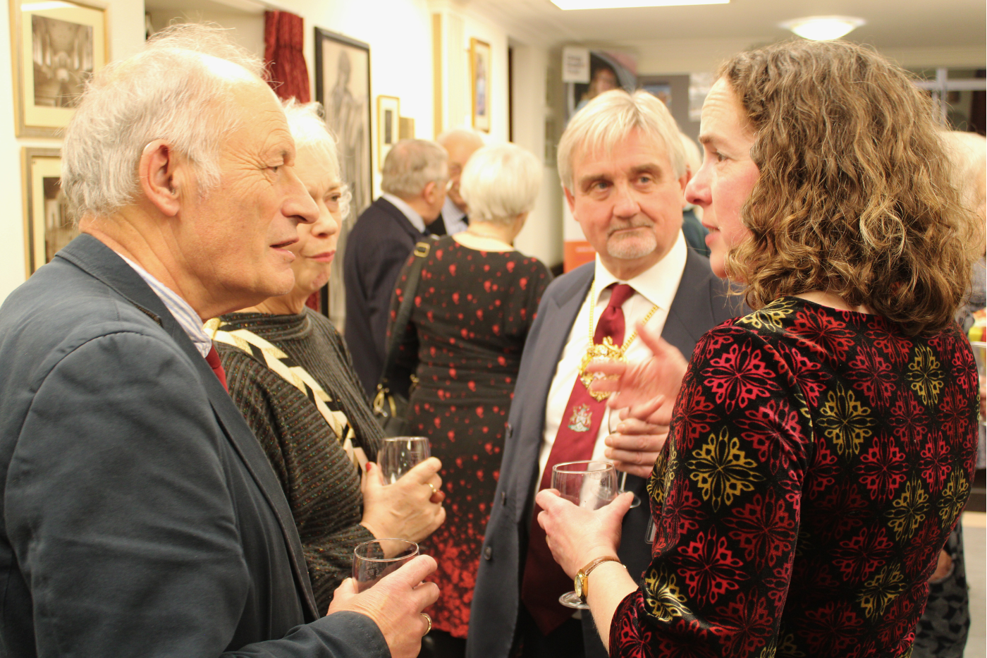 Four guests, dressed formally, in discussion over a glass of wine.