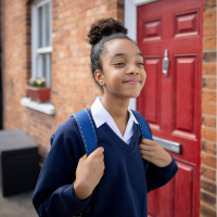 A girl walking to school. Her hair is in a bun, and she's holding the straps of her backpack.