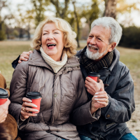 Two couples, sat beside each other on a park bench, enjoying hot drinks in takeaway cups.