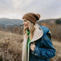 A woman enjoying a hike. She is wearing a brown bobble hat, and a blue jacket.